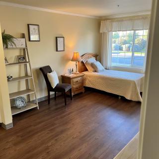 A cozy bedroom featuring a single bed, a bedside lamp, and a window with natural light.