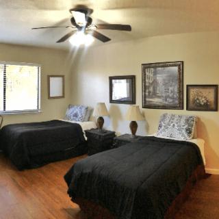 A cozy bedroom featuring two beds with black bedspreads, framed artwork on the walls, and a ceiling fan overhead.