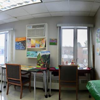A cozy workspace with artwork on the walls, featuring tables and chairs near large windows.