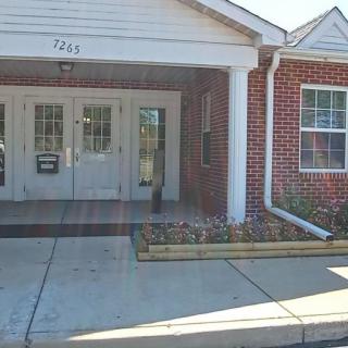 A brick building entrance with a double door and windows, featuring a small awning and adjacent flowerbed.
