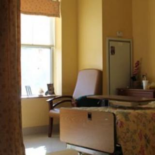 A hospital room with a bed, chair, and window.