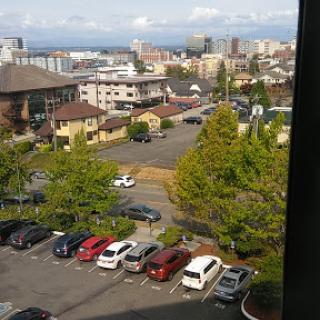 A view of a bustling city with a parking lot in the foreground and various buildings in the background.