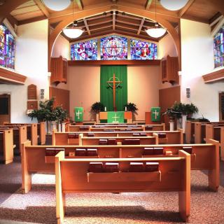 A church interior with wooden pews, stained glass windows, and a central altar featuring a cross.
