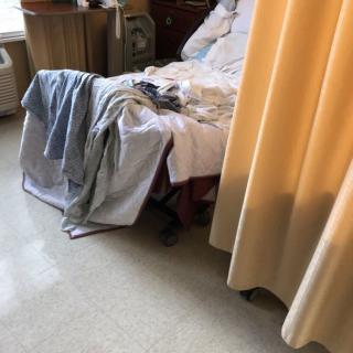 A hospital room with a bed, linens, and a privacy curtain.