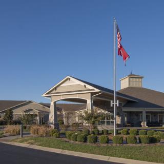A building with flags flying in front, surrounded by neatly trimmed landscaping on a clear day.