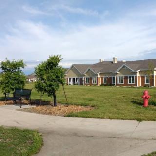 A wide view of a residential building with a lawn, trees, and a pathway leading to it under a cloudy sky.