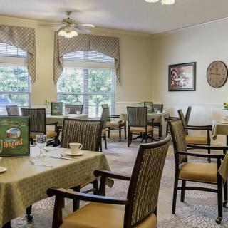 A cozy dining room with neatly arranged tables and chairs, featuring large windows and pleasant decor.