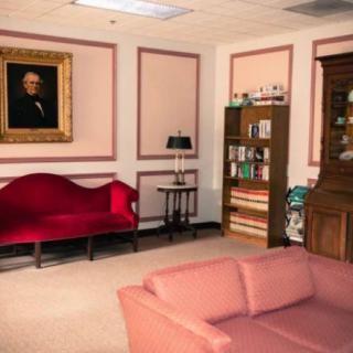 A classic living room with red and pink sofas, a bookshelf, and a portrait on the wall.