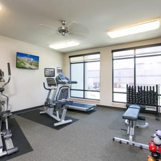 A well-equipped gym with various exercise machines and weights, brightly lit by natural light from large windows.