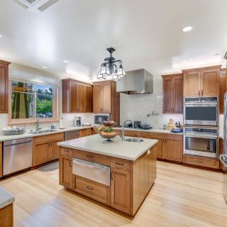 A spacious modern kitchen with wooden cabinetry and stainless steel appliances, featuring a central island and hardwood flooring.