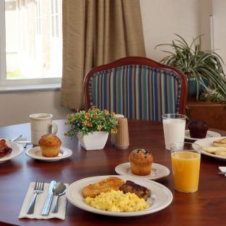 A table set for breakfast with eggs, toast, muffins, and drinks including orange juice, coffee, and milk.