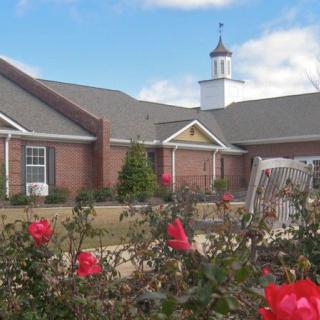 A picturesque brick building with a garden of red flowers under a blue sky.