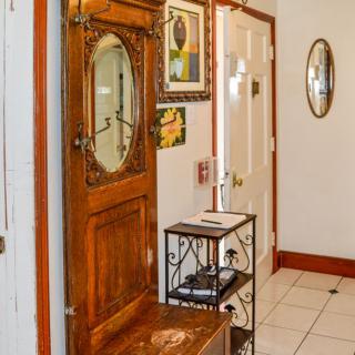 A cozy hallway featuring a wooden door with an oval mirror, decorated walls with artwork, and a small metal shelf on tiled flooring.