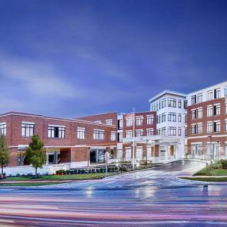 A modern brick building at night with illuminated windows and streaks of light from passing cars.