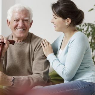 A young woman gently places her hand on an elderly man's shoulder, offering support and care.