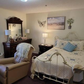 A cozy bedroom featuring a vintage-style bed, a comfortable armchair, and a wooden dresser with a mirror.