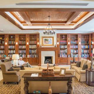 A luxurious library living room with extensive bookshelves, a cozy fireplace, and comfortable seating.