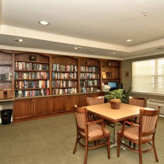 A cozy library room with bookshelves, a table, and chairs suitable for reading and studying.