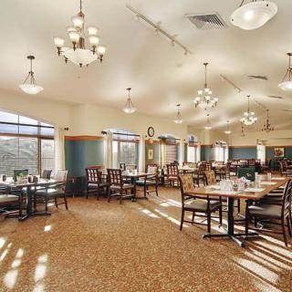 A spacious dining room with tables and chairs arranged under elegant chandeliers.