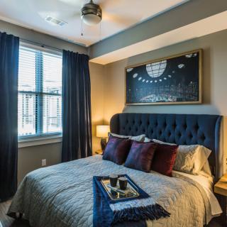 A cozy and stylishly decorated bedroom with a tufted headboard, dark curtains, and modern artwork.