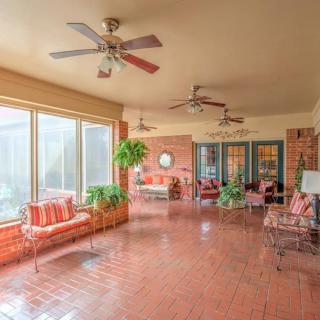 A spacious sunroom with brick flooring, ceiling fans, and large windows, featuring comfortable seating and potted plants.