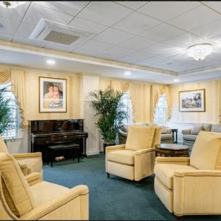 A well-appointed living room featuring comfortable chairs, a piano, and decorative artwork.