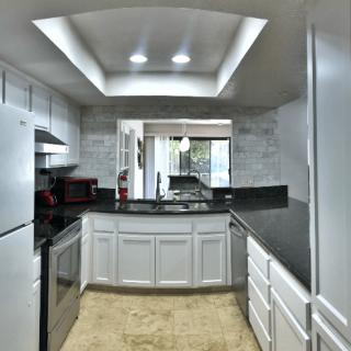 A modern kitchen featuring white cabinets and a black countertop with recessed lighting.