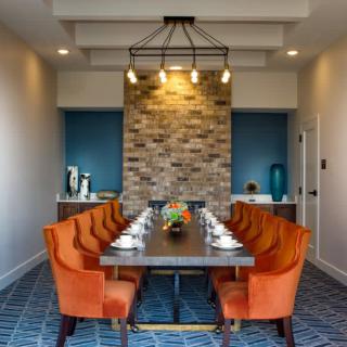 A modern dining room with orange chairs and a brick accent wall.