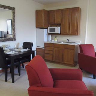 A cozy living space with a kitchenette, featuring red armchairs and a small dining area.
