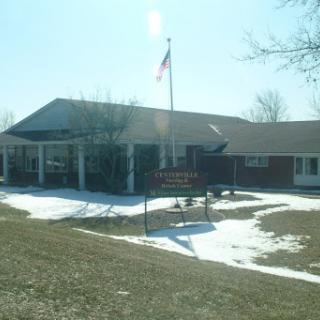 A building with a flag standing in front, surrounded by snow and grass on a sunny day.