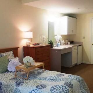 A cozy bedroom with a bed, dresser, and a small kitchenette area.