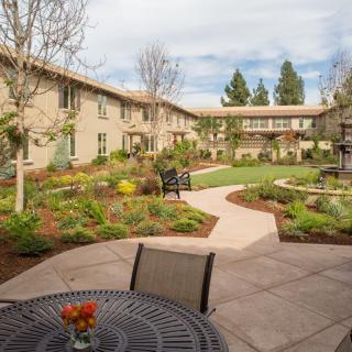 A tranquil courtyard with a garden path and seating area, surrounded by a two-story building.