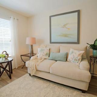A cozy living room with a beige sofa adorned with pillows, a side table with a lamp, and a painting on the wall.