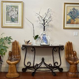 A stylish interior arrangement featuring a decorative table with a vase and plant, flanked by unique hand-shaped chairs and framed artwork on the wall.