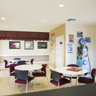 A well-lit waiting room with round tables and chairs, decorated with vintage posters.