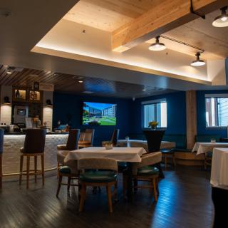 A modern restaurant interior with tables, seating, and a bar area.