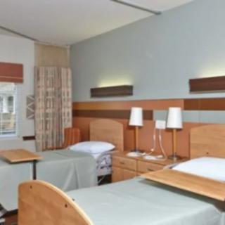 A hospital room with two beds, equipped with lamps and a curtain divider.