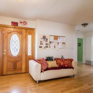 A cozy living room with a sofa and wooden flooring, featuring an entrance area adorned with a decorative door and notice board.