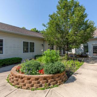 A well-maintained garden with a central brick planter and a tree, surrounded by a residential building.