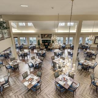 A spacious and elegantly designed dining area with neatly arranged tables and chairs under warm chandeliers.