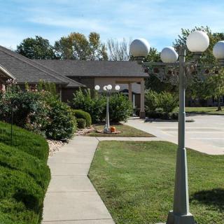 A scenic view of a building entrance with a landscaped pathway and street lamps on a clear day.