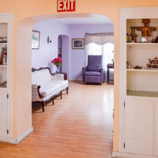 A cozy living room with a sofa, armchair, and wooden flooring, featuring an exit sign above the archway.