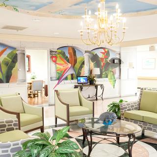 A bright and inviting lobby with green upholstered chairs, vibrant artwork on the walls, and a chandelier overhead.