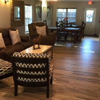 A cozy living room with sofas and chairs arranged around a wooden table on a hardwood floor.