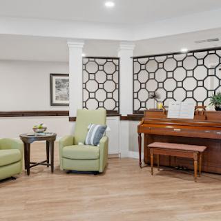 A cozy lounge area featuring comfortable green chairs and a wooden piano, adorned with decorative accents.