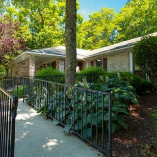 A charming single-story house surrounded by lush greenery and a paved walkway.