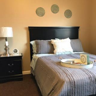 A cozy bedroom with a neatly made bed, bedside table, and decorative elements on the wall.