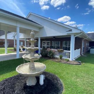 A small garden with a multi-tiered fountain in front of a house on a sunny day.