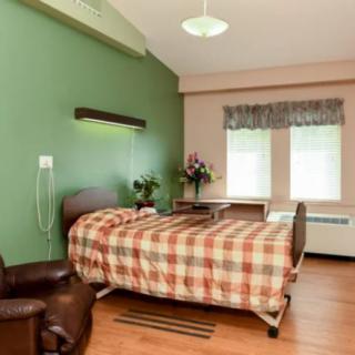 A neat hospital room with a single bed, green accent wall, and a comfortable chair.