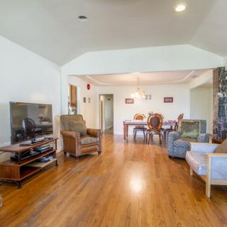 A spacious living room with wood flooring and a dining area in the background, featuring comfortable seating and a television.